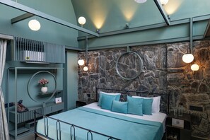 A modern bedroom with a stone wall, a bed with blue bedding, and circular wall sconces.