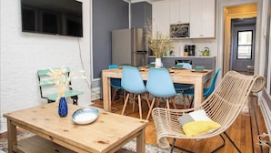 A modern kitchen with a dining area, including a wooden table, blue chairs, and a wicker chair. - Modern 4-Bedroom Stay in the Heart of Lenox Hill! (New York)