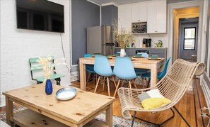 Een moderne keuken met een eethoek, met een houten tafel, blauwe stoelen en een rieten stoel.