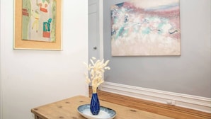 A wooden table with a vase of dried plants and a framed abstract painting on the wall. - Modern 4-Bedroom Stay in the Heart of Lenox Hill! (New York)