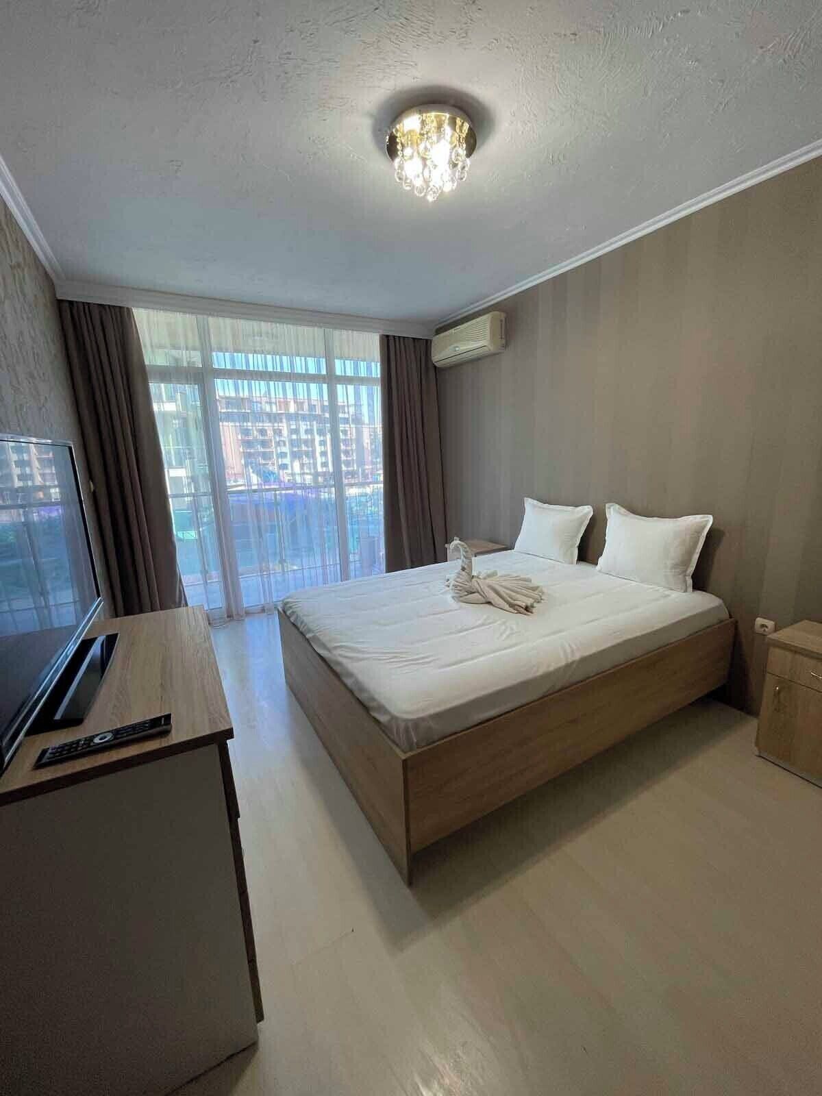 A hotel room with a bed, a desk with a TV, and a window with curtains.