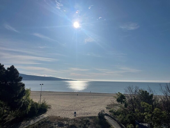 A beach with a clear sky, a sun shining, and a distant mountain. - 2-bedroom apartment in amazing Sunny Beach,beachfront location,sea views (Sunny Beach)