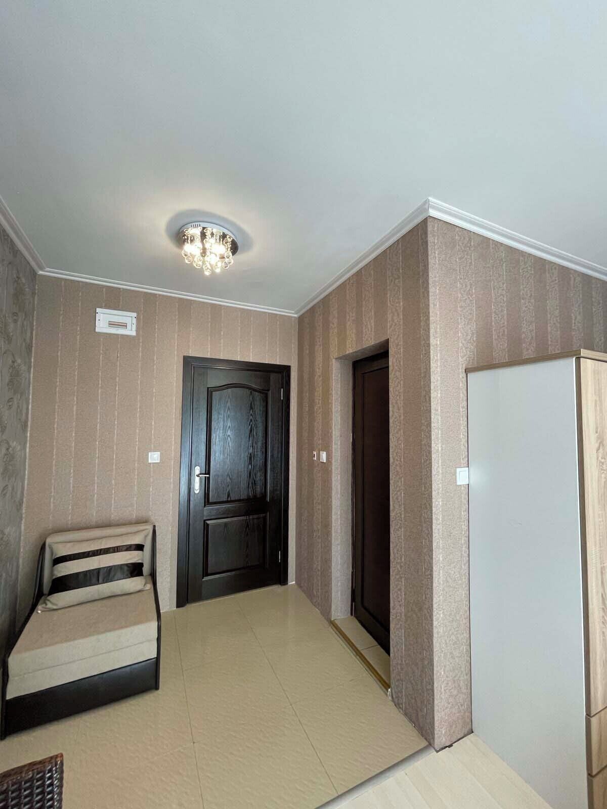 A room with a dark wooden door, a white refrigerator, and a beige sofa.