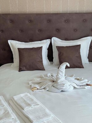 Una cama bien hecha, con un cabecero marrón, dos almohadas blancas y una toalla blanca colocada sobre la cama.