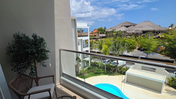 A balcony with wicker furniture, a view of a swimming pool, and buildings with thatched roofs in the background. - Laguna Beach 405- 300m from Dominicus Public Beach (Dominicus)