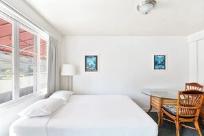 Ein Hotelzimmer mit Bett, Tisch, zwei Stühlen, einem Fenster mit Vorhängen und zwei gerahmten Bildern an der Wand.