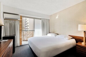 Ein Hotelzimmer mit Bett, Schreibtisch, Klimaanlage, Lampe und Blick auf einen Balkon.
