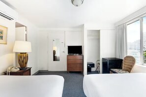 Ein Hotelzimmer mit zwei Betten, einem Schreibtisch mit Fernseher, einem Kleiderschrank und einem Fenster mit Blick.