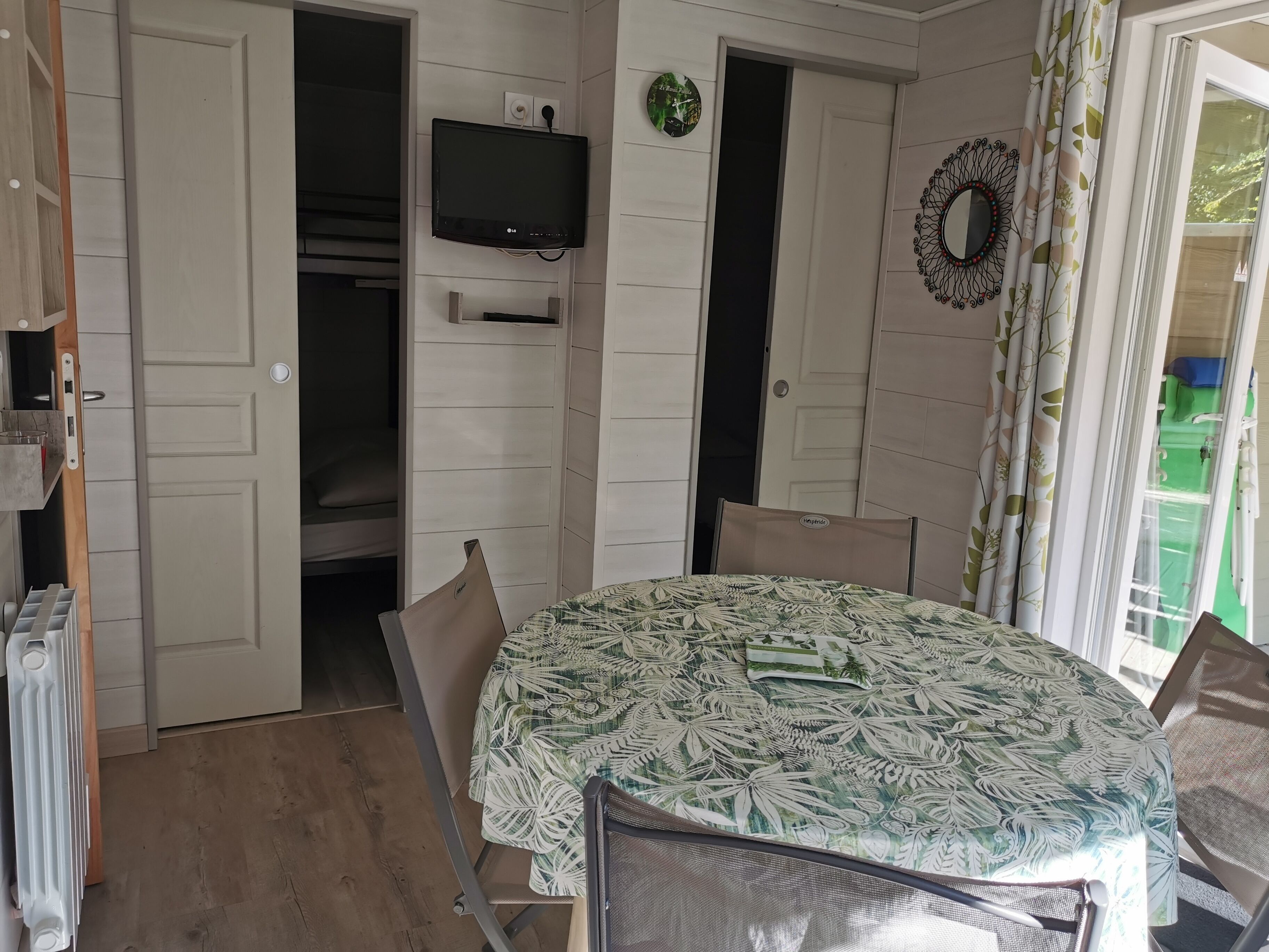 Een kamer met een ronde tafel, stoelen, een televisie, een klok en een deur naar een andere kamer.