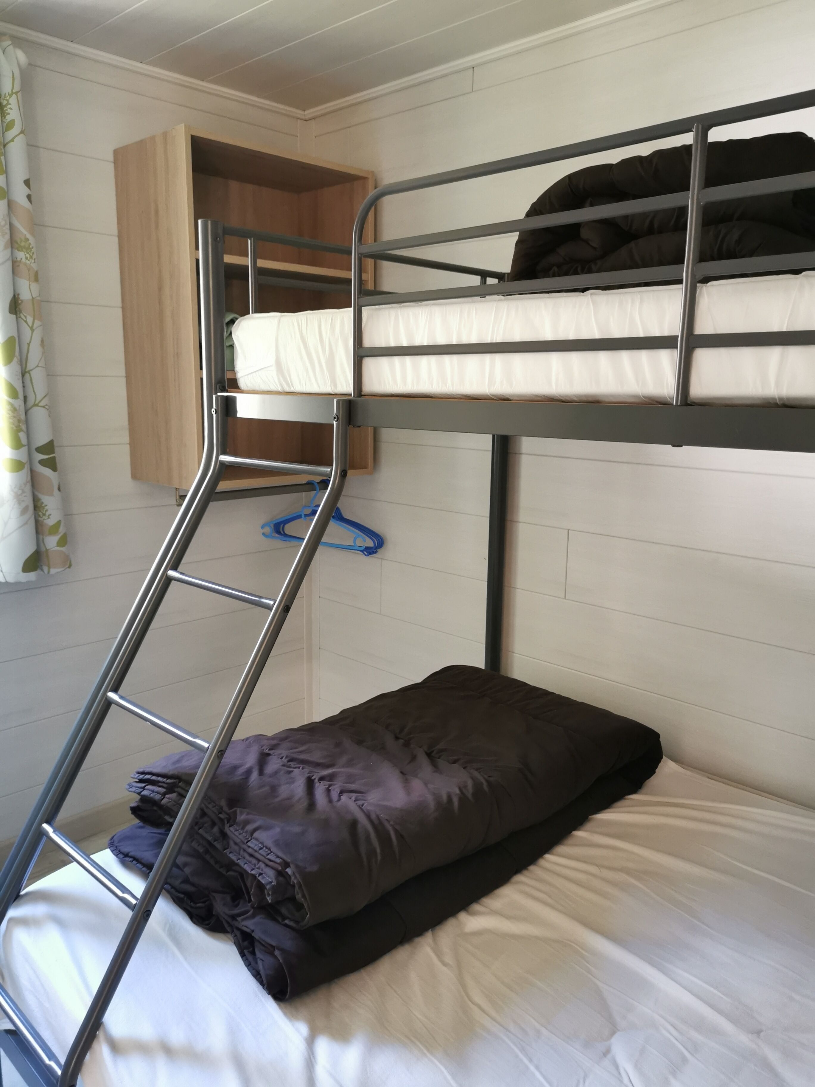 A bunk bed with a ladder, a wooden shelf, and a blue hanger.