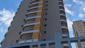 Een hoog gebouw met meerdere balkons, een heldere lucht en een gedeeltelijk zicht op een ander gebouw.