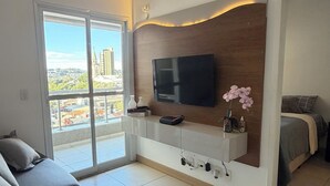 Een moderne woonkamer met een flatscreen televisie aan een houten wand, een bank en een bed met uitzicht op de stad.