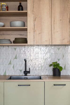 A kitchen with a sink, wooden cabinets, and a tiled backsplash. - Stunning Designer Apartment in the Heart of Paris (11th Arrondissement) (Paris)