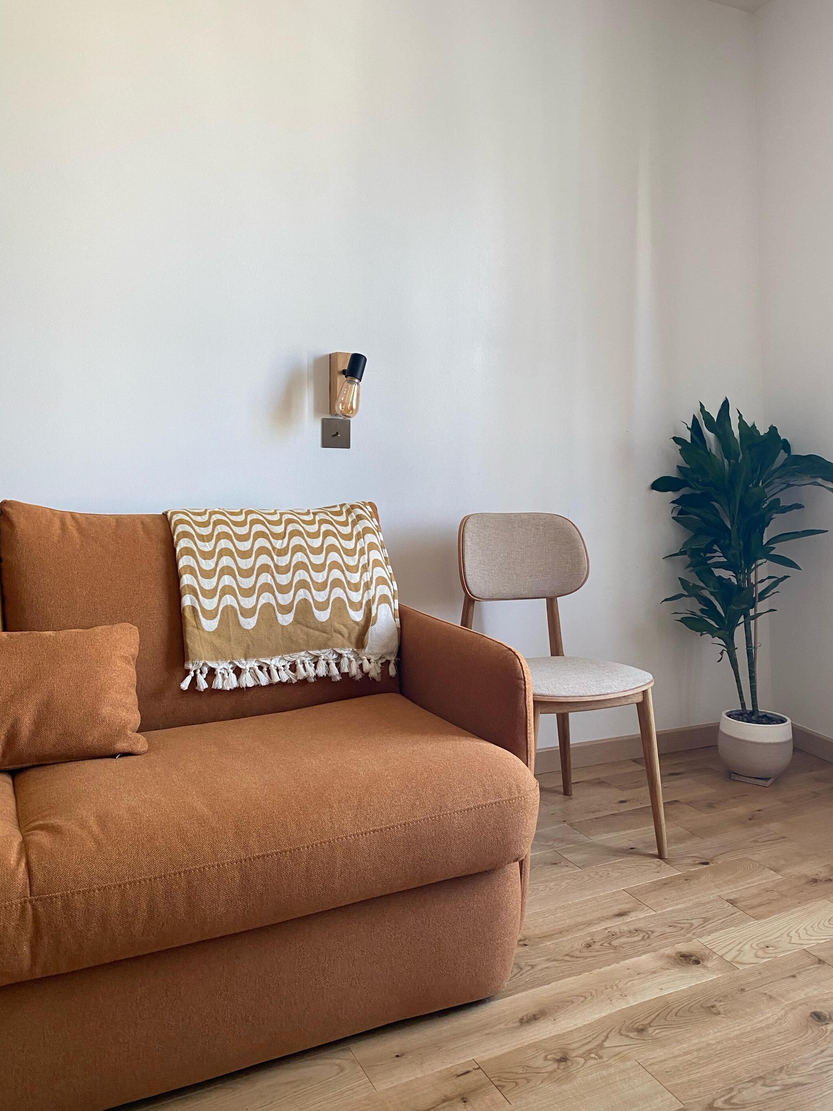 A room with a sofa, a chair, a potted plant, and a wall-mounted light fixture.