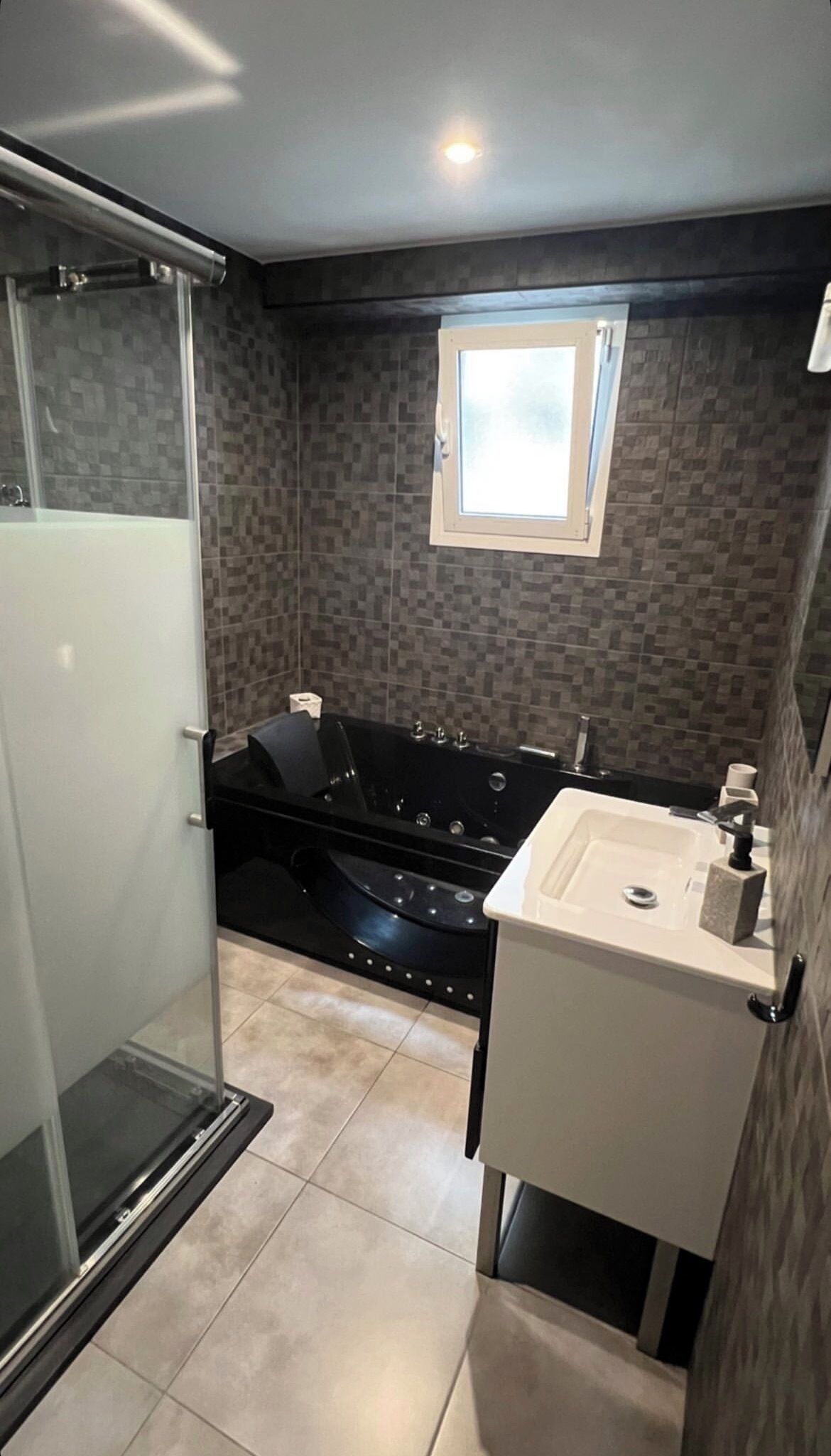 Een moderne badkamer met een glazen douchecabine, een zwart whirlpoolbad en een witte wastafel met spiegel.