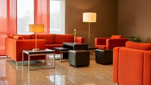 Un hall d’entrée moderne avec des canapés orange, une table basse, un lampadaire et une plante en pot.