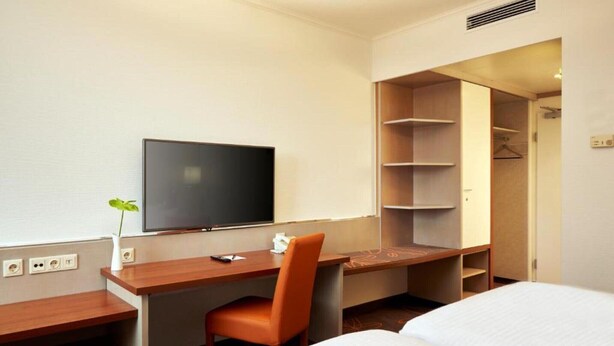 Une chambre d’hôtel comprenant un lit, un bureau avec une chaise, une télévision et un dressing.