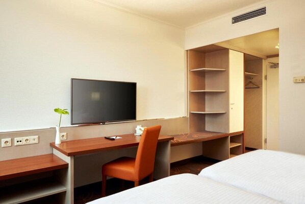 A hotel room with a bed, a desk with a chair, a television, and a walk-in closet.