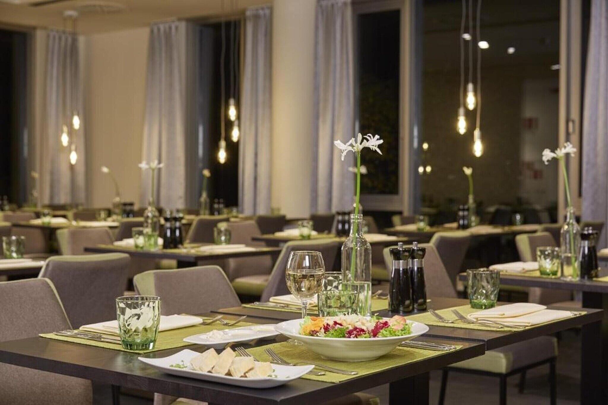 Ein Restaurant mit gedeckten Tischen, auf jedem Tisch ein Teller Essen, ein Glas Wasser und eine Weinflasche.