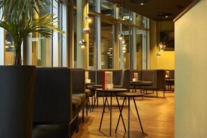 Rebedor modern d'hotel amb zones d'estar, una planta gran en test i il·luminació penjant.