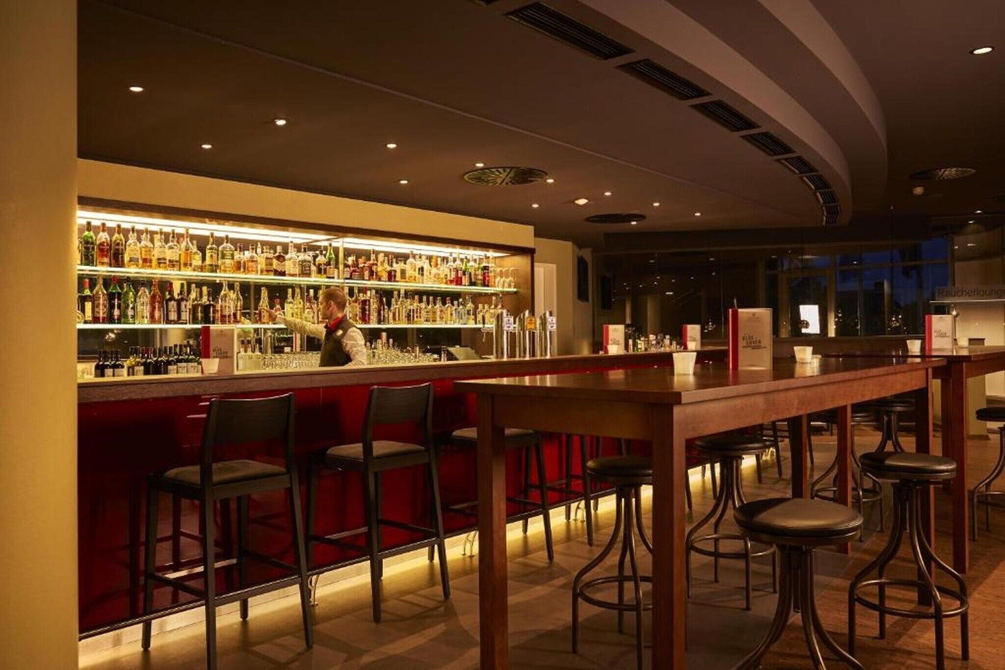 Eine Bar mit Bartender, einer gut sortierten Spirituosenregal und mehreren Barhocker.