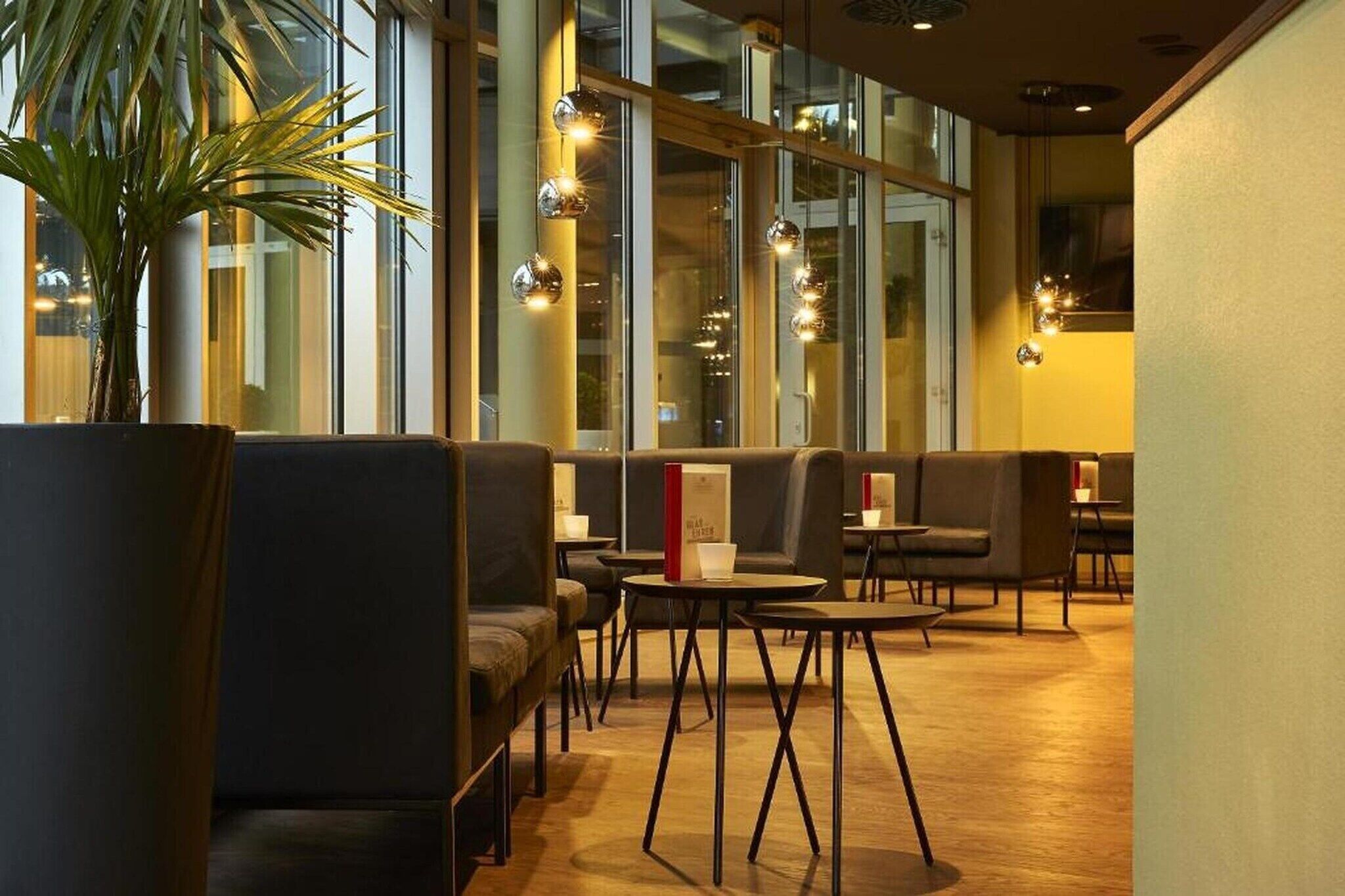 Eine moderne Hotelhalle mit Sitzbereichen, einer großen Küstpflanze und Pendelleuchten.