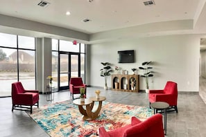A spacious lobby with large windows, red chairs, a round wooden coffee table, and a flat-screen TV mounted on the wall. - 2 Queen Beds|Mobil Access|RI Shr|Ktchn (Houston)