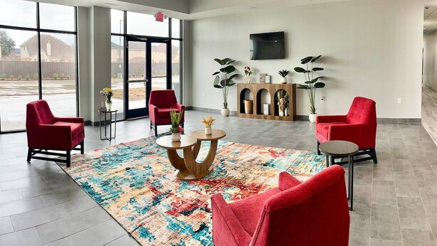Eine geräumige Lobby mit großen Fenstern, roten Sesseln, einem runden Tisch in der Mitte und einem an der Wand befestigten Fernseher.