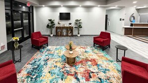 Eine Lobby mit farbenfrohem Teppich, roten Sesseln, einem hölzernen Couchtisch, einem an der Wand montierten Fernseher und einer Rezeption.