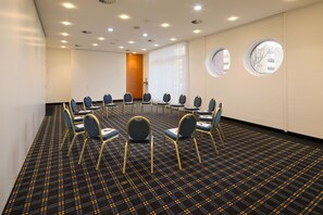 Ein Konferenzraum mit rundem Tisch, blauen Stühlen und einem gemusterten Teppich.