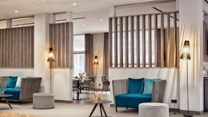 A modern hotel lobby with a seating area, a dining area, and a kitchen in the background. - Sunday Hotel Köln Hürth Disability Access (Hürth)