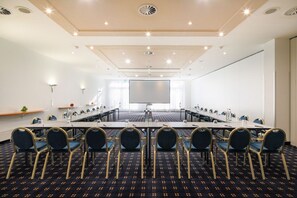 Ein Konferenzraum mit einem langen Tisch, Stühlen, einer Projektionsleinwand und einem Teppichboden.