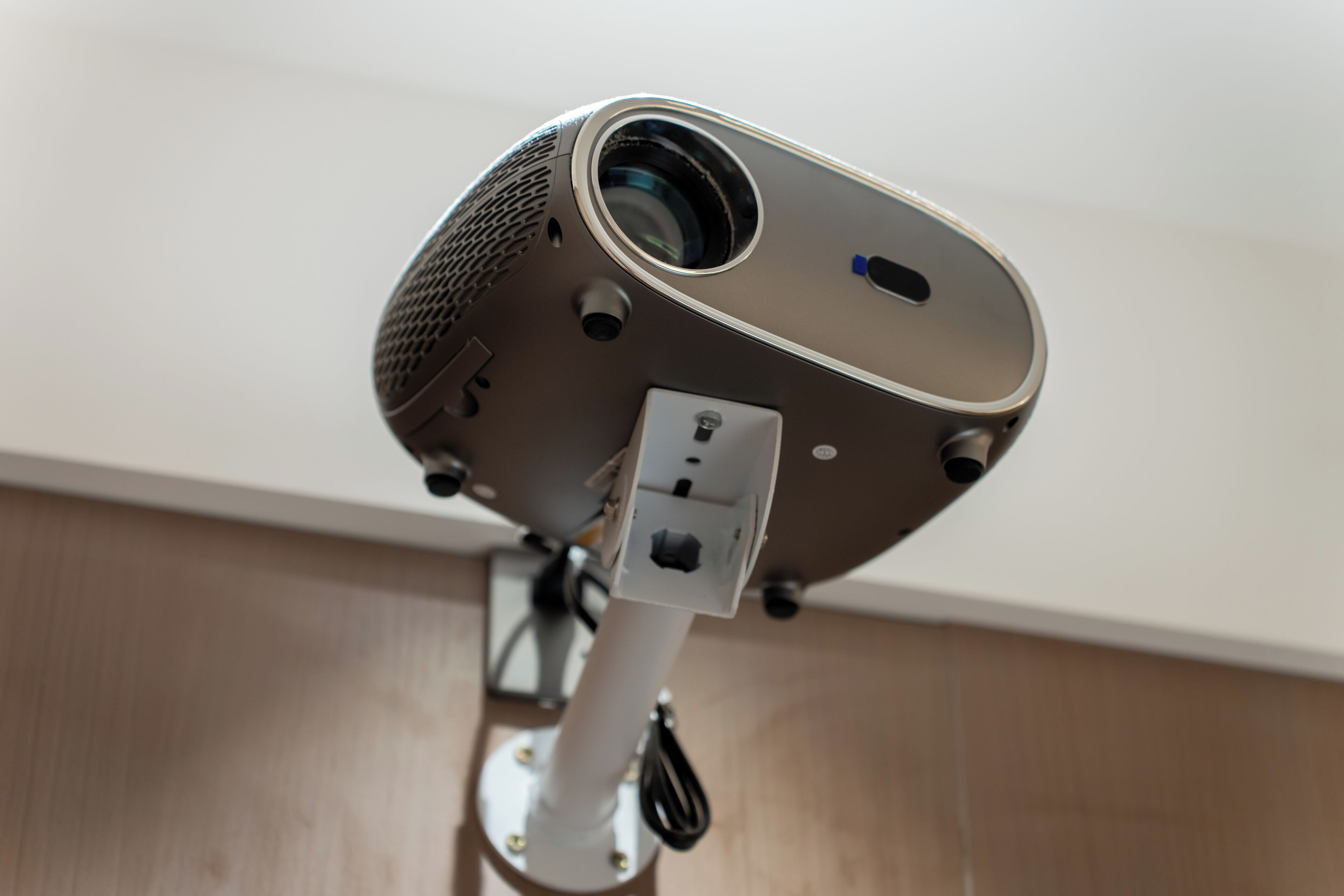 Un proyector fijado al techo, con lente, ventilación y cable de alimentación.