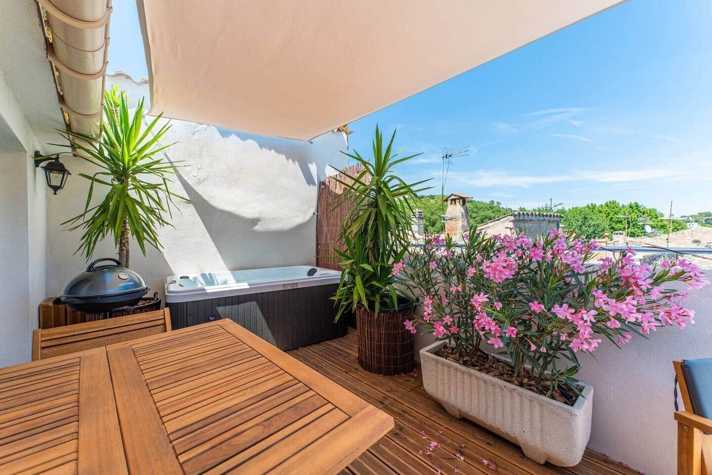 Una terraza en la azotea con una mesa de madera, un jacuzzi y plantas en macetas.