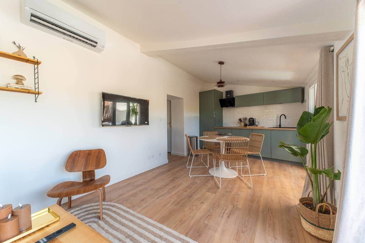 Una cocina moderna con gabinetes verdes, un comedor con sillas de mimbre y una planta grande.
