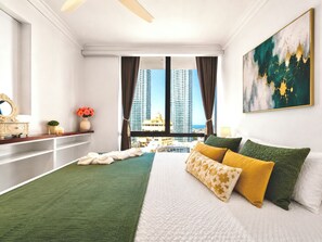 Habitación de hotel con cama, vista de edificios altos, un cuadro y una tocador con espejo.