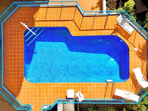 A rectangular swimming pool with a tiled deck, surrounded by a blue metal railing, and equipped with white lounge chairs and a sunbed. - Robin's Oceanview Penthouse | 1 Min to Beach (Surfers Paradise)