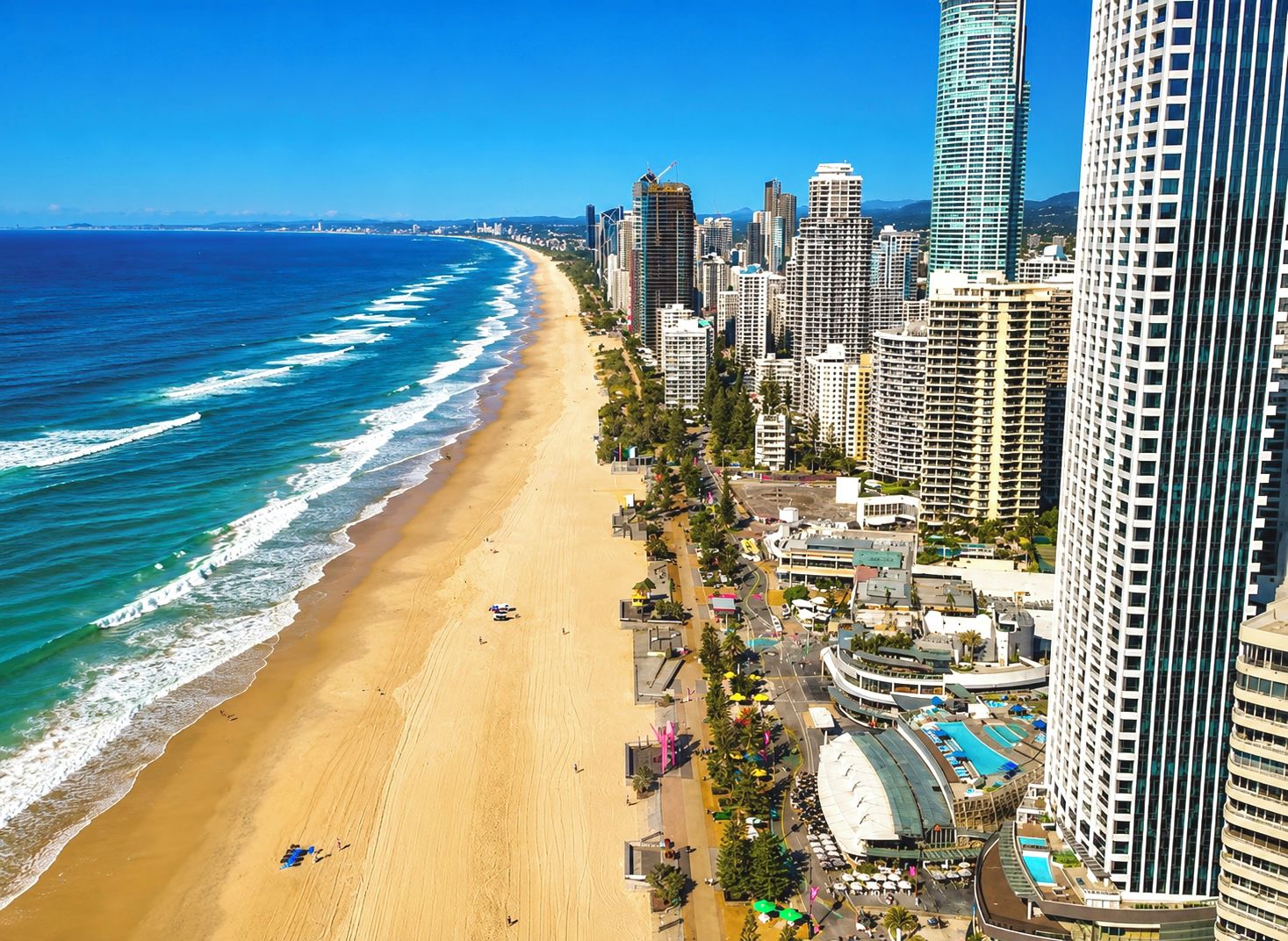 Eine Küstenstadt mit Strand, Hochhäusern und einem großen Hotelkomplex mit Pool.