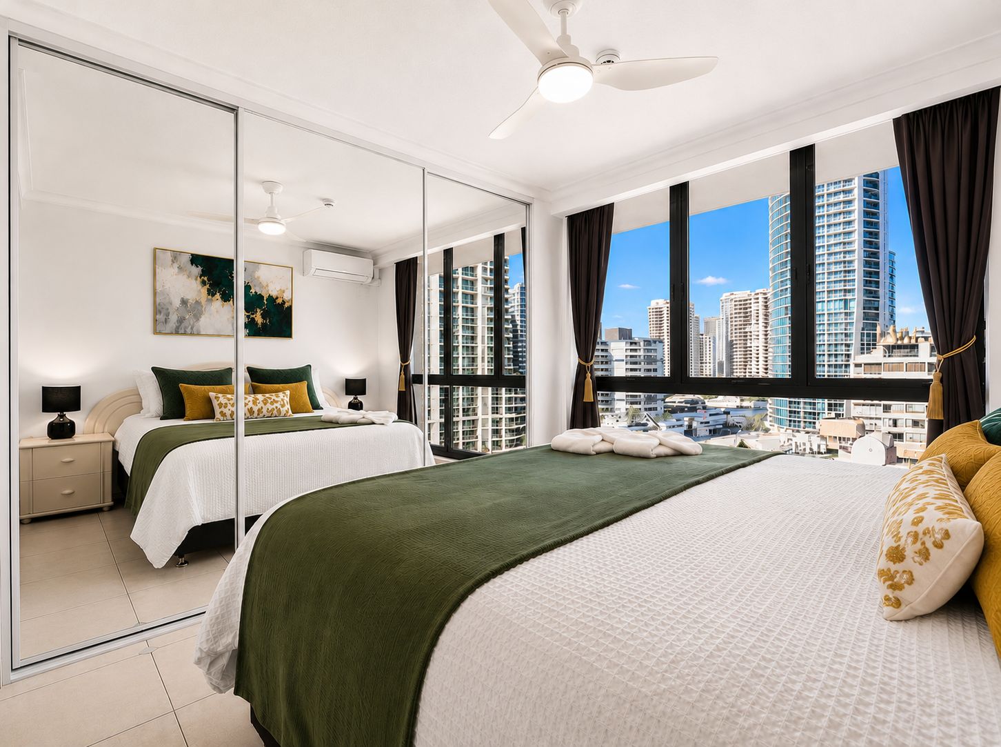 Une chambre d’hôtel moderne avec un grand lit, un miroir, un ventilateur de plafond et une vue sur la ville.