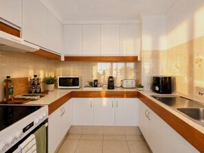 A modern kitchen with white cabinets, a microwave, toaster, coffee maker, and a stove. - Robin's Oceanview Penthouse | 1 Min to Beach (Surfers Paradise)