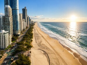 Paisatge urbà costaner amb edificis alts, una platja ampla i sorrenca, i un cel serè.