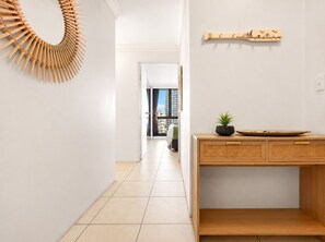 Un pasillo con un cuadro de madera, una consola de madera con una planta y un estante de pared con objetos decorativos.