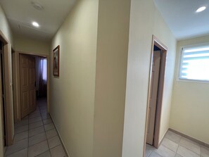 Ein Flur mit einer Tür zu einem Zimmer, einem Fenster mit Jalousien und einem gefliesten Boden.