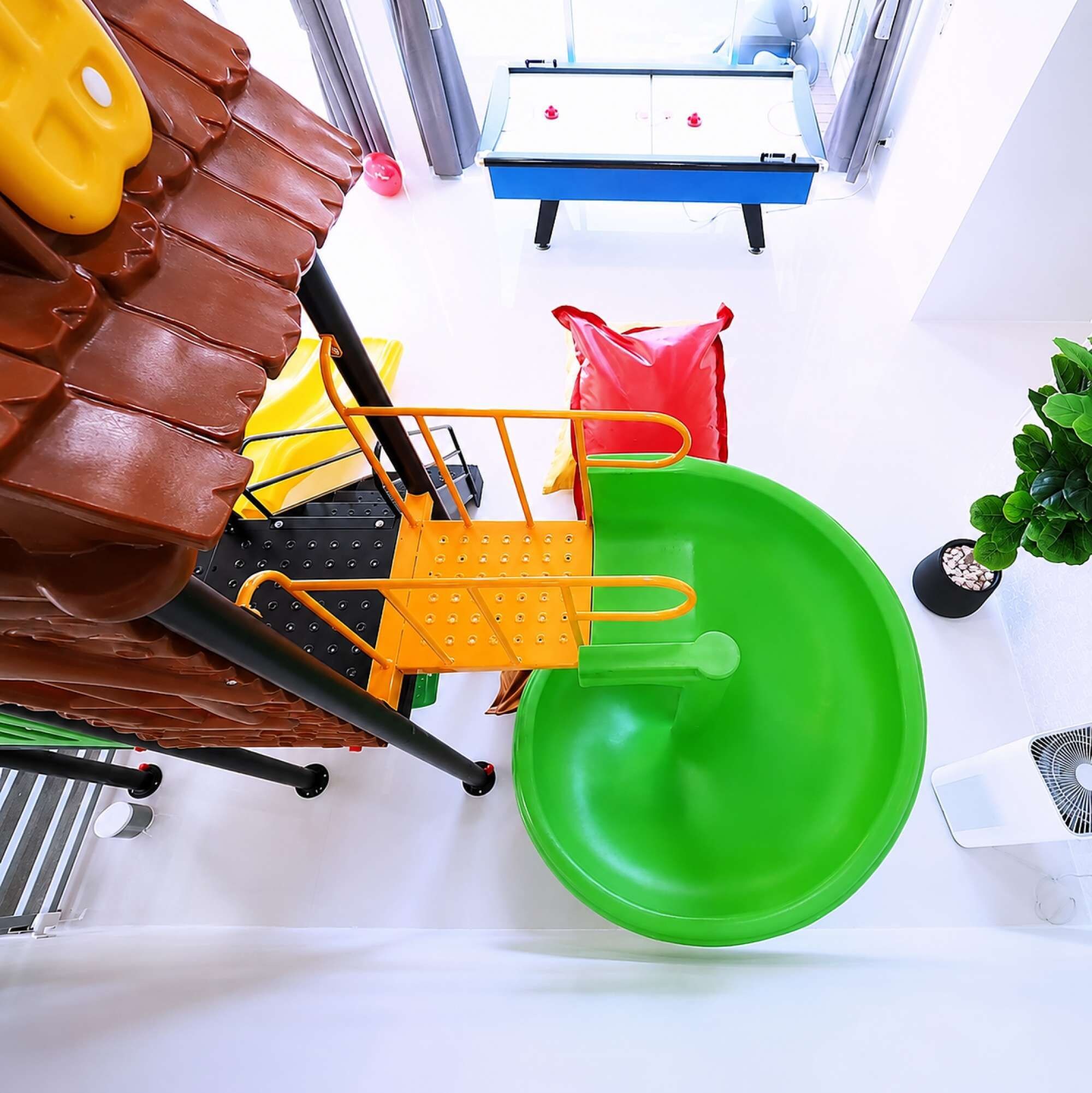 A room with a green plastic chair, a yellow chair, a brown leather chair, a red bag, and a blue table with a white surface.
