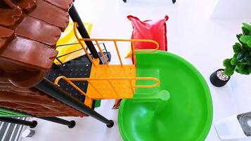 A room with a green plastic chair, a yellow chair, a brown leather chair, a red bag, and a blue table with a white surface.