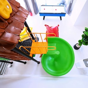 A room with a green plastic chair, a yellow chair, a brown leather chair, a red bag, and a blue table with a white surface. - 3-Bedroom Private Pool Villa for Up to 10 Guests (Si Racha)