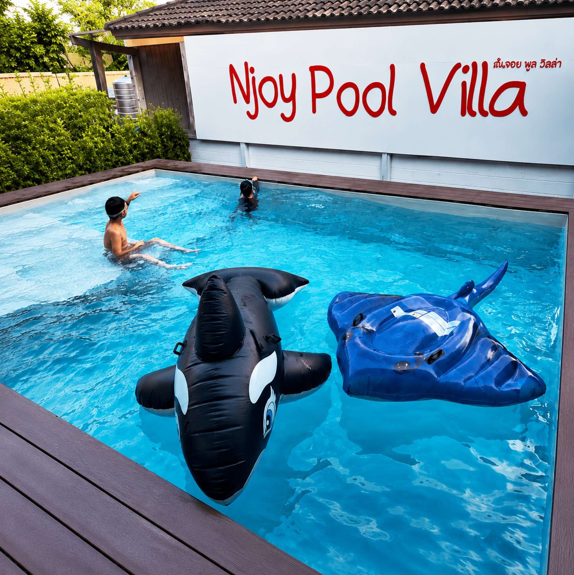 Una piscina con juguetes inflables de orca y raya, y un letrero que dice 'Njoy Pool Villa'.