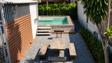 A rectangular swimming pool with a wooden deck and benches, surrounded by a gravel area and a low brick wall.