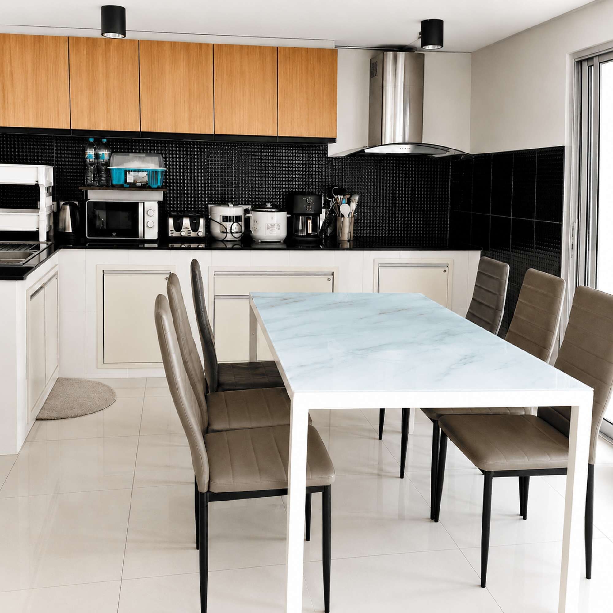 A modern kitchen with a marble dining table, built-in appliances, and a black backsplash.