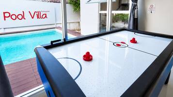 A pool table with a clear view of a swimming pool outside, a sign reading 'Pool Villa', and a window with curtains.